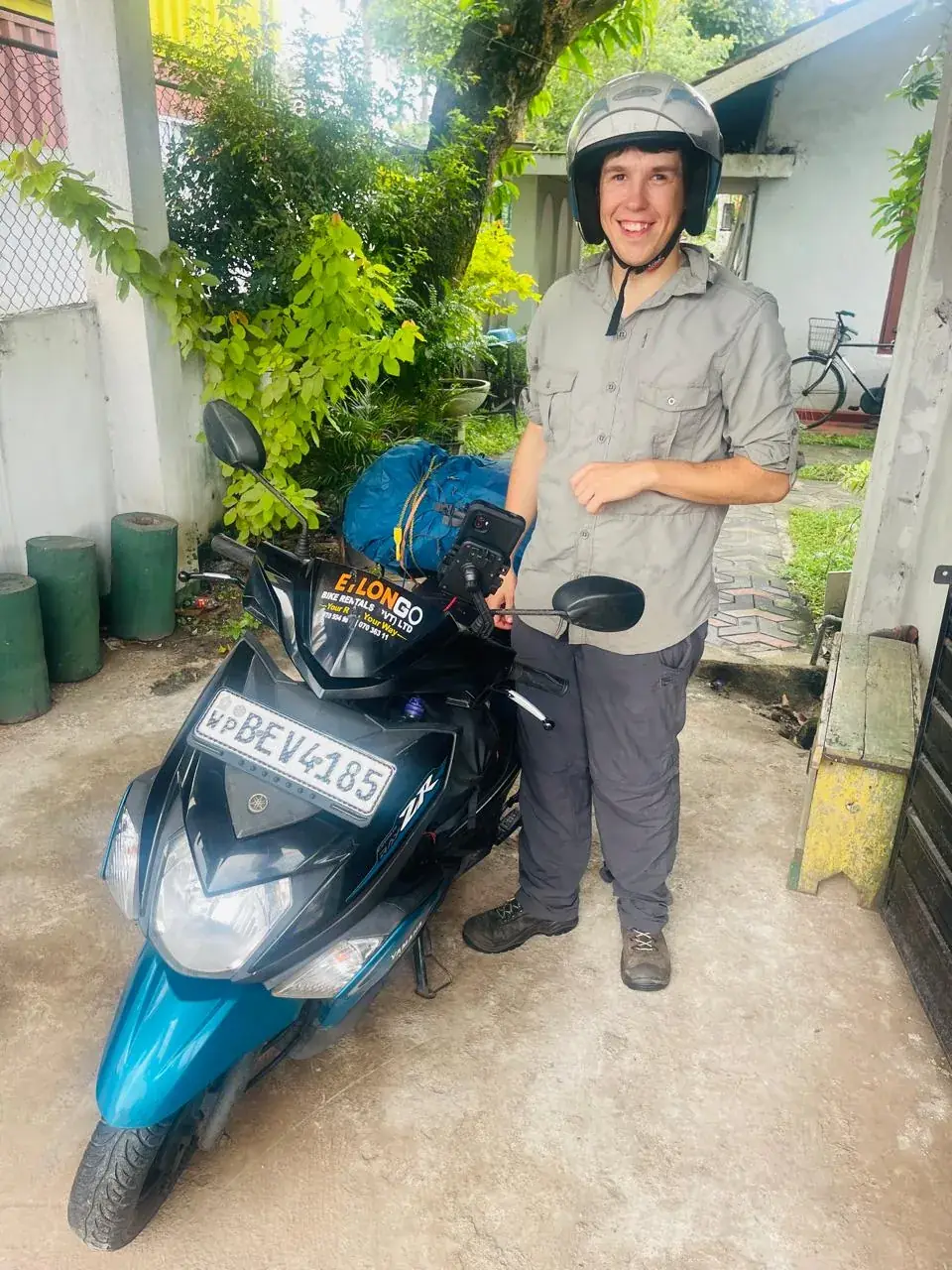 Smiling traveller in a helmet beside a CeylonGo Yamaha Ray ZR with luggage