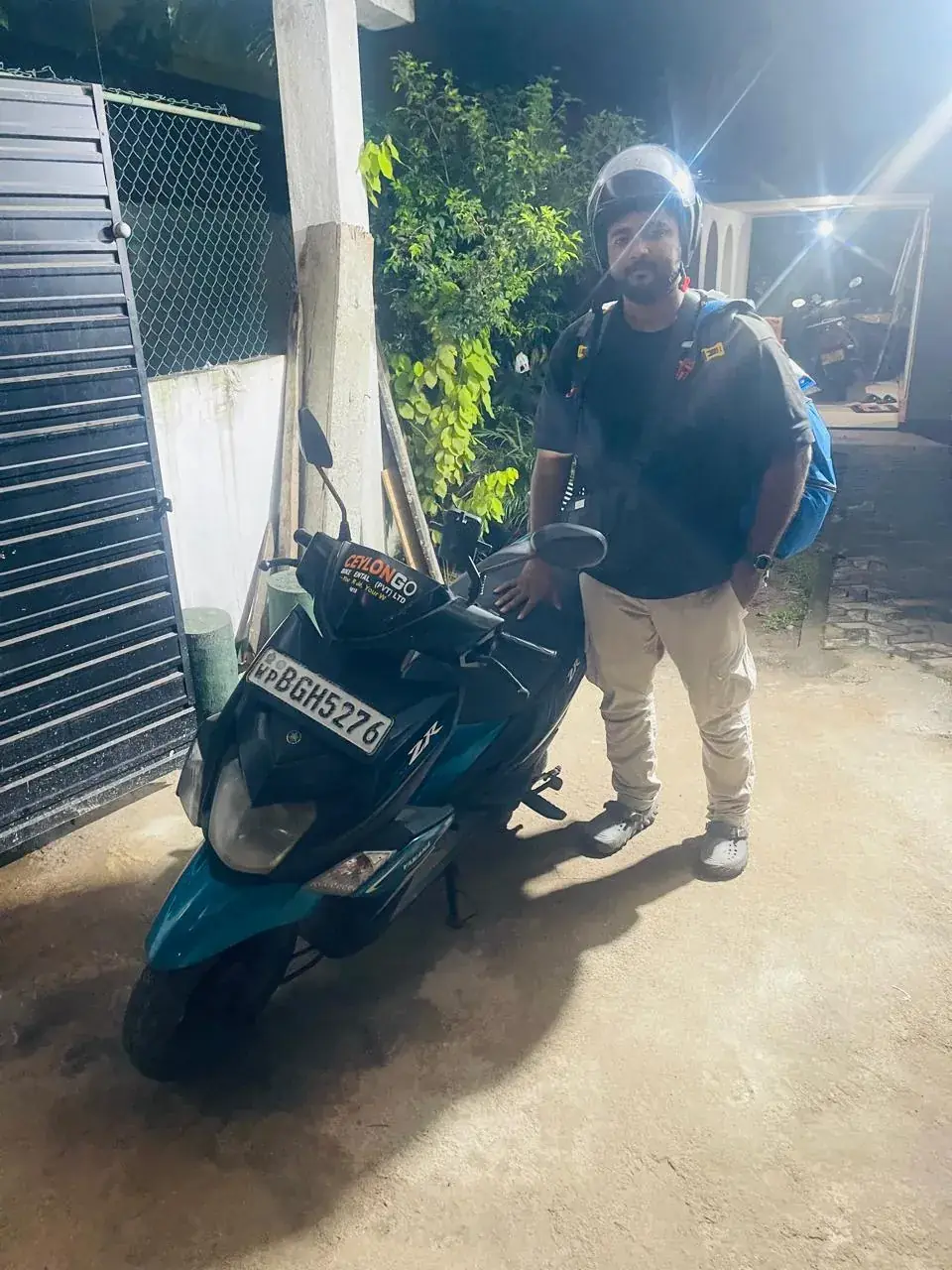 Traveller standing beside a CeylonGo Yamaha Ray ZR scooter at night